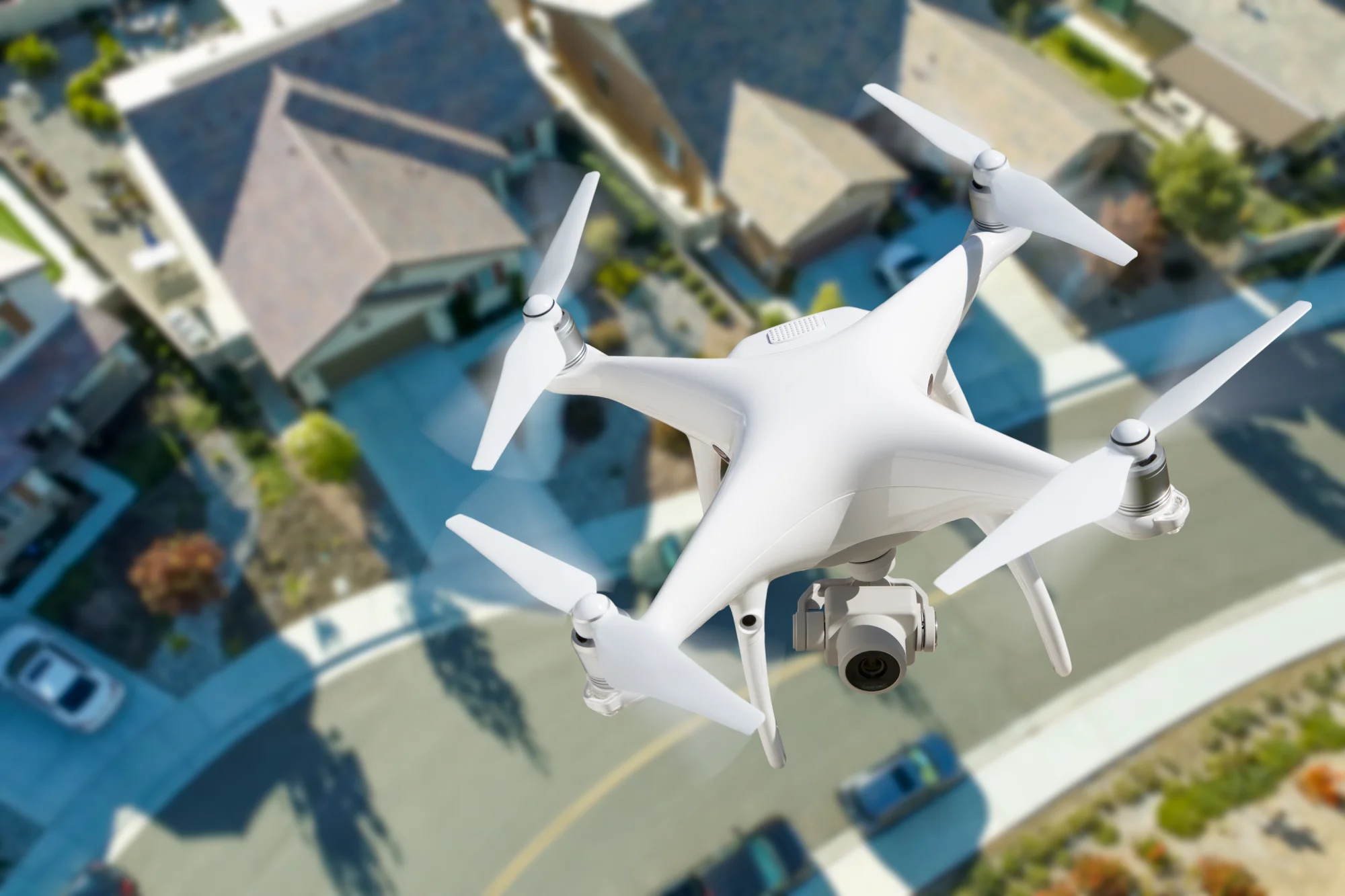 Un drone quadricoptère blanc planant au-dessus d'un quartier résidentiel, capturant des vues aériennes des maisons et des rues en contrebas.